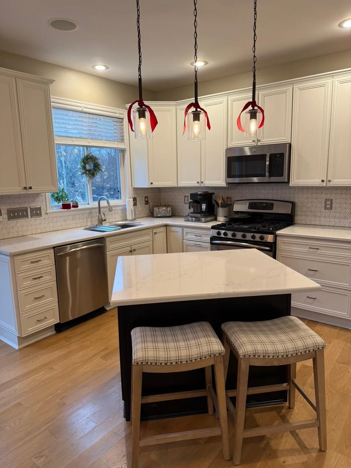 Refinished white kitchen cabinets and island with dark pendant lights.